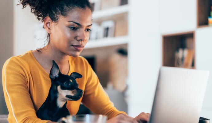 Vrouw aan een laptop met een hond op schoot