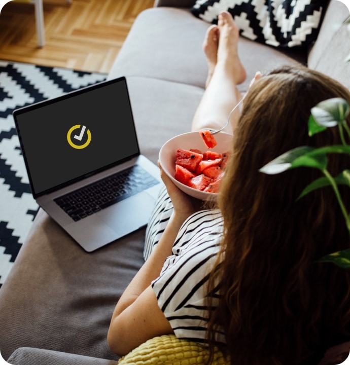 Vrouw die fruit eet met laptop naast haar waarop het symbool van Gen Digital is te zien.